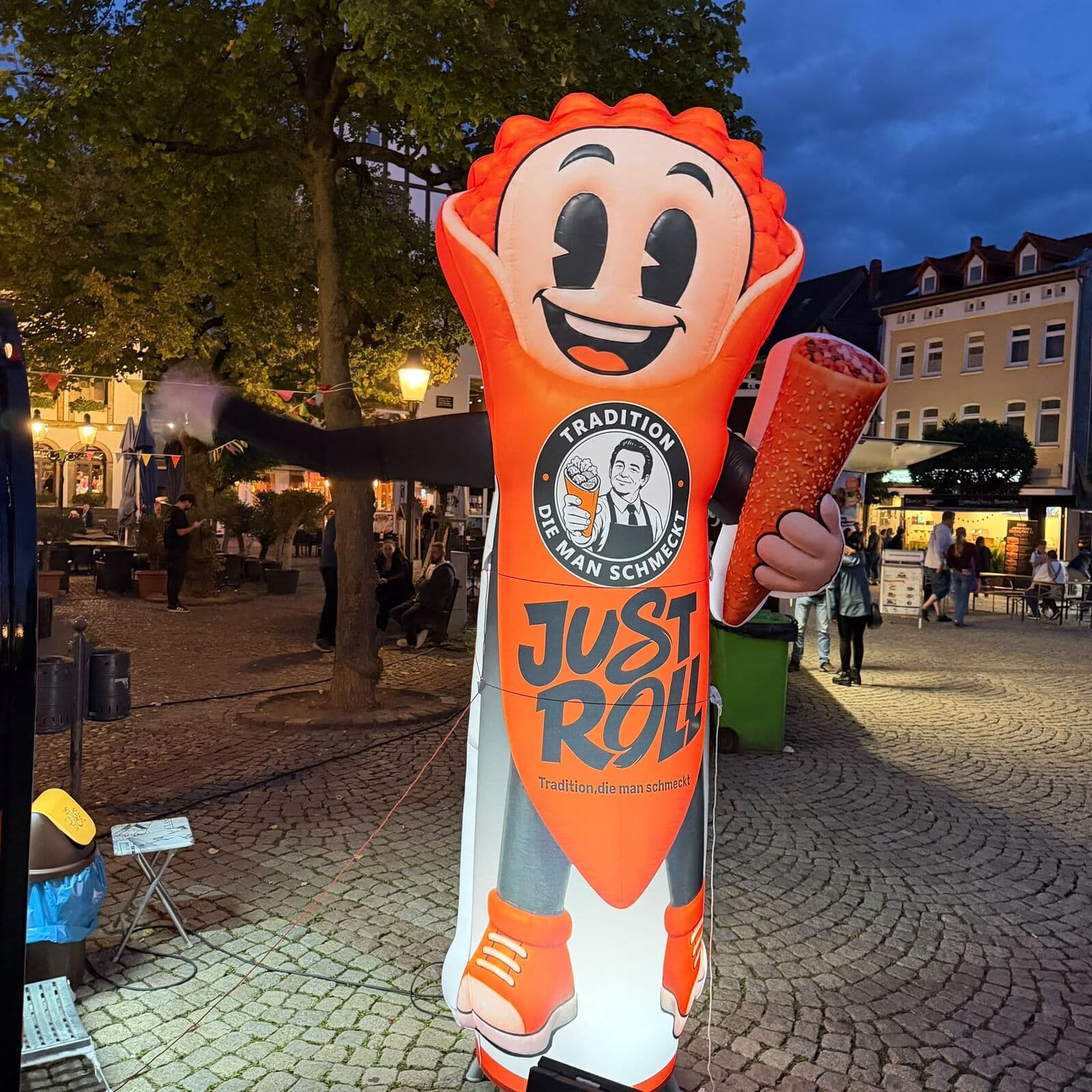 Aufblasbares Just-Roll-Maskottchen mit einer Roll in der Hand auf einem Platz am Abend