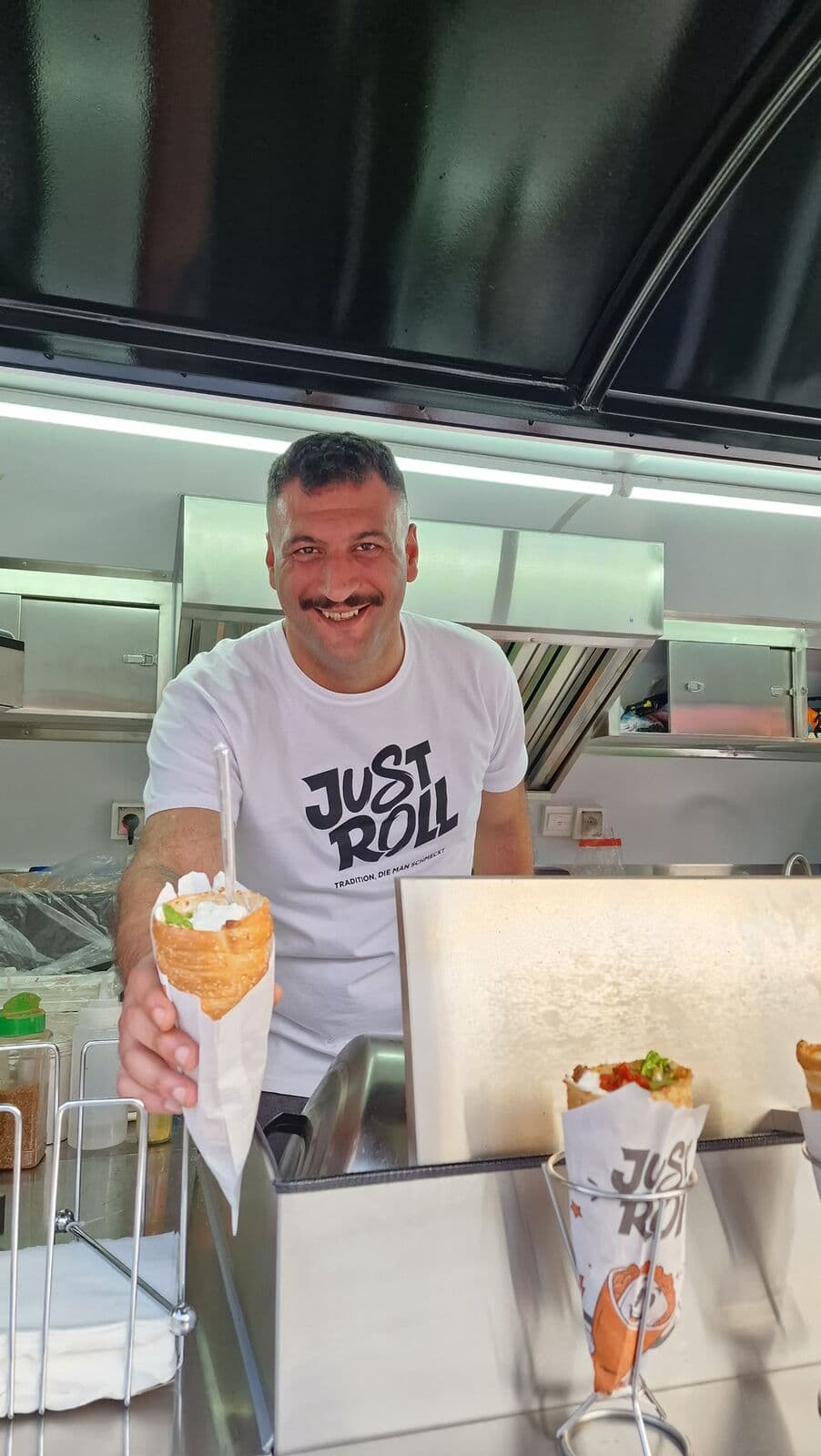 Mitarbeiter im Just-Roll-Shirt reicht eine gefüllte Roll über die Theke