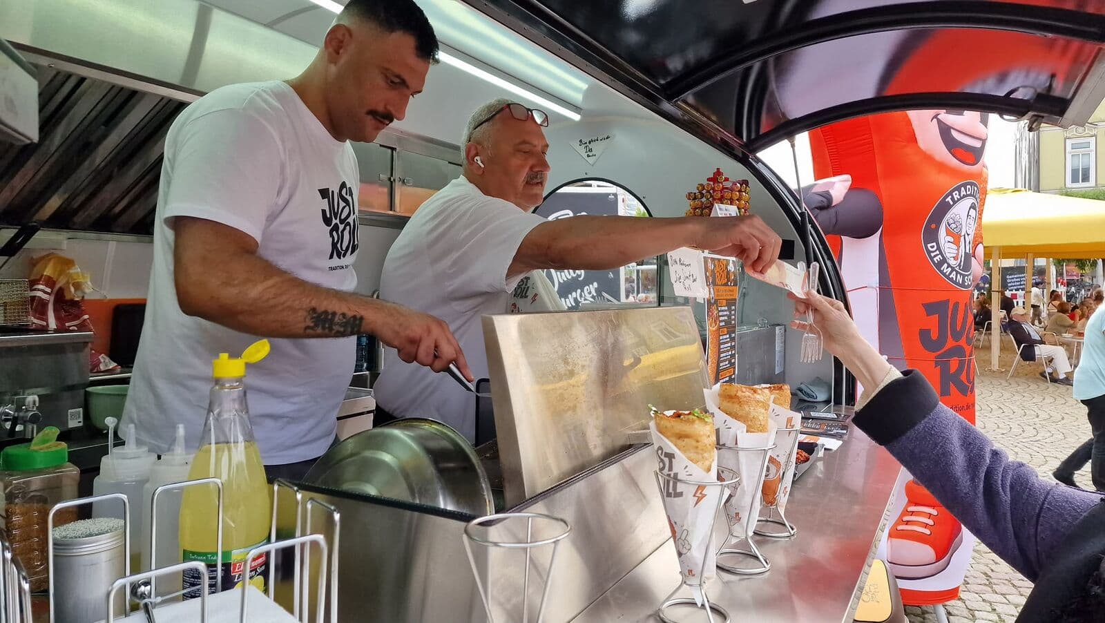 Zwei Mitarbeiter in Just-Roll-Shirts füllen Rolls an der Ausgabe des Trailers