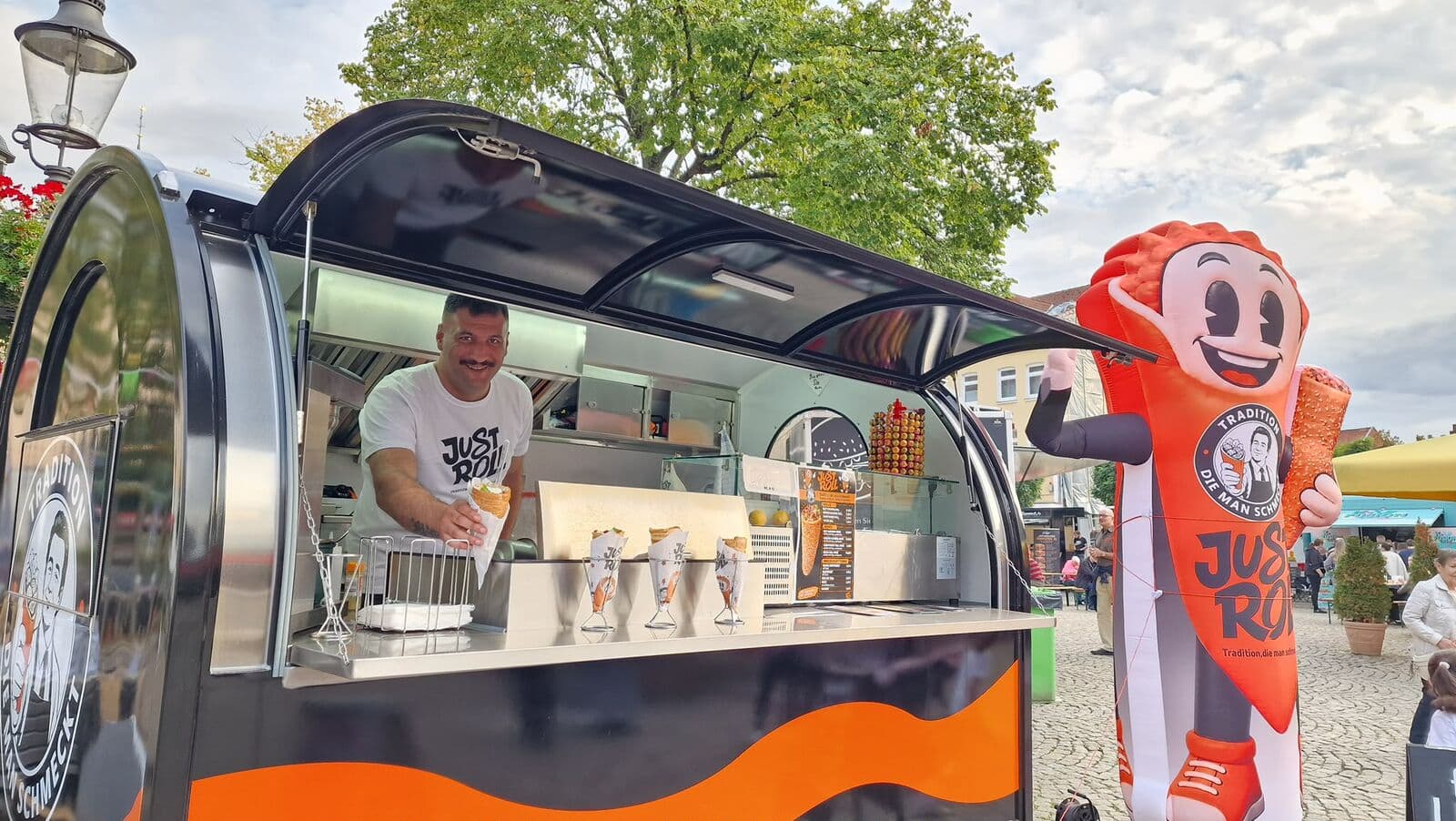 Geöffnete Ausgabeklappe des Just-Roll-Trailers mit Maskottchen daneben