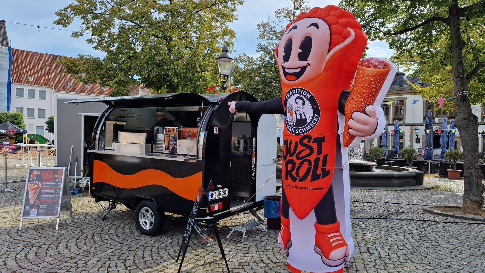 Just-Roll-Trailer mit Maskottchen auf einem Marktplatz bei Tag